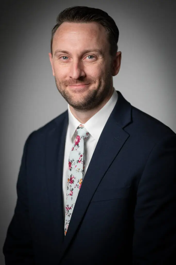 Kyle Martinos, Electroneuromyographer and physical therapist with EMG Solutions in a suit and tie smiling with gray background